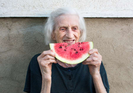 Cheerful grandma eating watermelon fruit in the backyardの写真素材