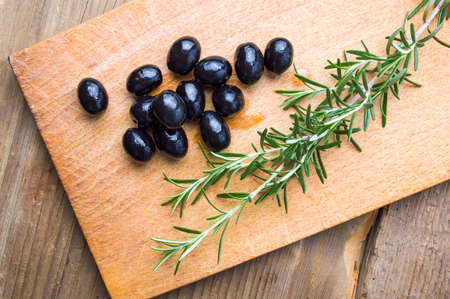 Dark olives and rosemary plant on a cutting boardの写真素材