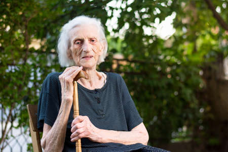Senior woman sitting with a walking cane outdoorsの写真素材