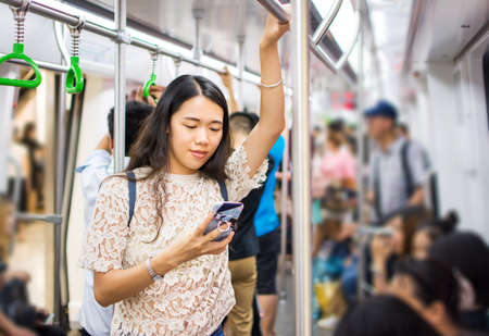 Asian girl using phone on busy subway trainの写真素材