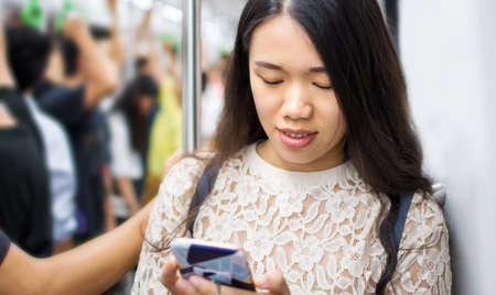 Asian girl using phone on busy subway trainの写真素材