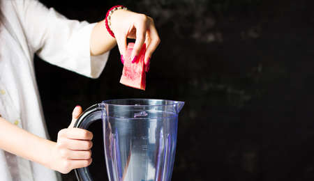 Female inserting watermelon slices in a blender to make a smoothieの写真素材