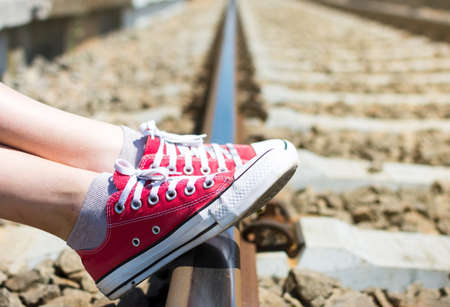 Girl feet in red sneakers sitting by the railroadの写真素材