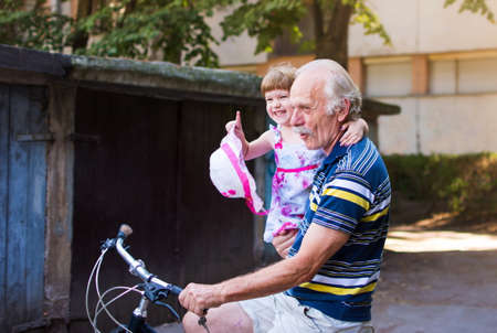 Grandpa riding bicycle with granddaughter in his handsの写真素材