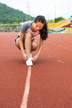 Girl tightening shoelaces on a jogging track before workoutの写真素材