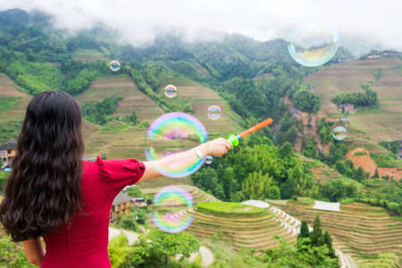 Girl making soap bubbles at rice terrace viewpoint wearing red dressの写真素材