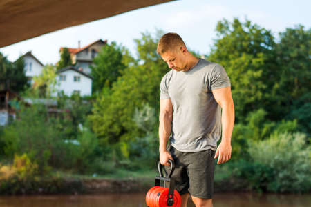 Masculine man with dumbbell by the river