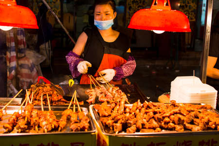NANNING, CHINA - JUNE 9, 2017: Chinese chef preparing barbecue on the Zhongshan Snack Street, a food market in Nanning. This food street is the biggest night food market  in the capital city of Guangxi province in Chinaのeditorial素材