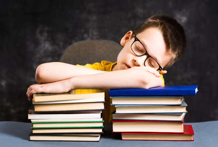 Tired school kid sleepeing on top of booksの写真素材