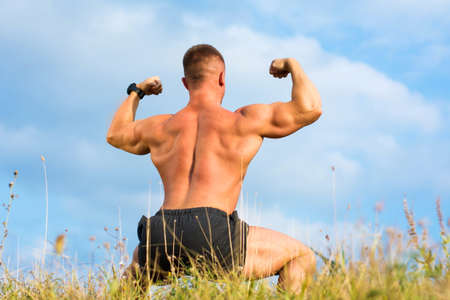 Bodybuilder flexing back muscles outdoors against blue sky