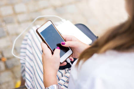 Girl using smart phone while charging on the power bankの写真素材