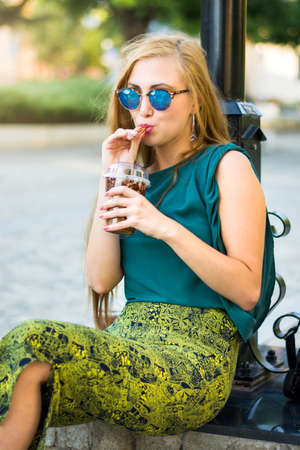 Fashionable girl sitting on the street and drinking coffee to goの写真素材