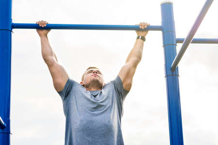 Masculine man doing pull ups on street workout outdoors