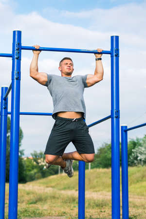 Masculine man doing pull ups on street workout outdoors