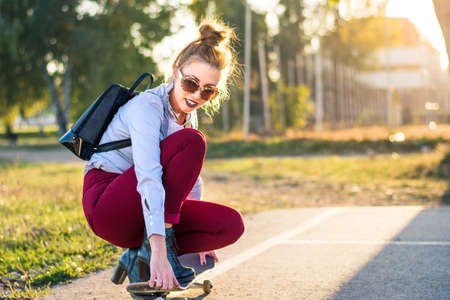 Fashionable girl with a skateboard in the park at sunset