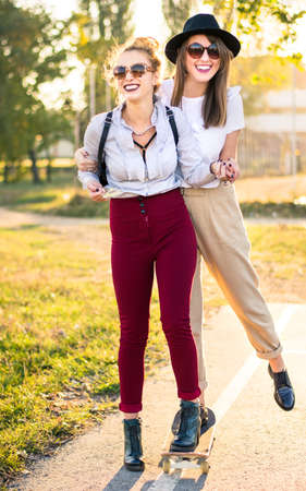 Two girls having fun with a skateboard in the parkの写真素材