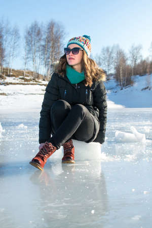 Girl sitting on ice cube on a frozen lake surfaceの写真素材