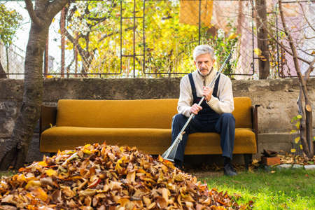 Tired senior man taking rest from cleaning fallen autumn leaves in the yardの写真素材