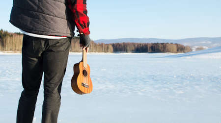 Man with ukulele standing on a frozen lake の写真素材