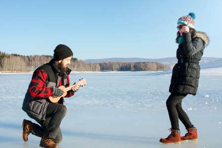 Man playing ukelele for his girlfriend on a frozen lake の写真素材