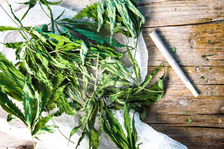 Dried marijuana leafs and a joint on a wooden tableの写真素材