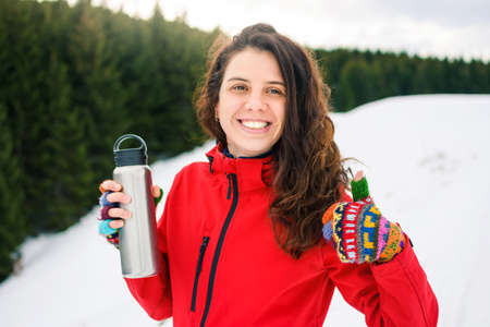 Happy female hiker with thermos on snowy mountainの写真素材