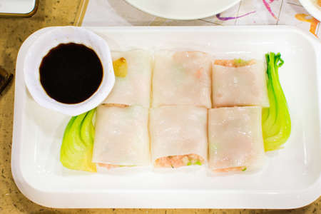 Steam rice noodle roll stuffed with pork and vegetable served on white plate on table