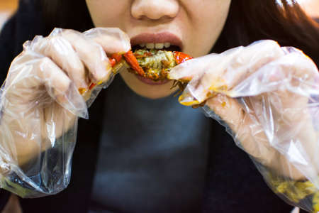 Asian woman eating a crayfish with plastic glovesの写真素材