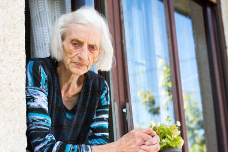 Pensive grandma in her 90s at the home window aloneの写真素材