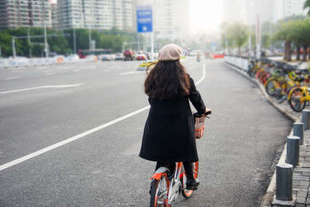 Asian office lady riding public bicycle through urban area の写真素材