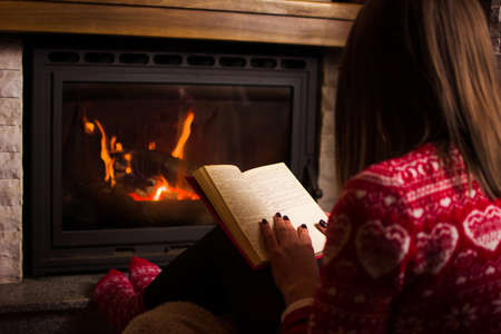 Woman reading by the fireplace at cold winter nightの写真素材