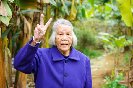 Cheerful senior asian woman showing V gesture outdoorsの写真素材