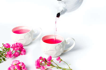 Person pouring tea with rose flowers on white tableの写真素材