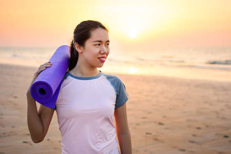 Happy girl with yoga mat on the beach for outdoors workoutの写真素材