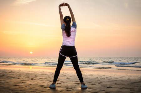 Girl exercising on the beach at sunset, outdoors workoutの写真素材