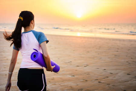 Girl with yoga mat on the beach for outdoors workoutの写真素材