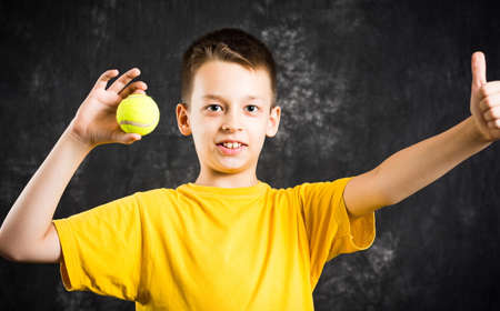 Happy teenage boy holding a tennis ball against dark backgroundの写真素材
