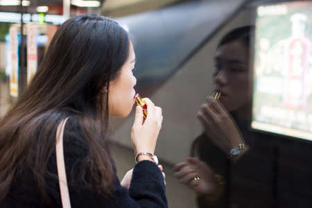 Girl applying lipstick while waiting for the metro at subway station
