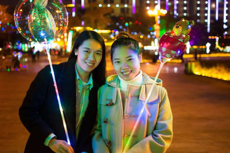 Friends with illuminated balloons in the city at nightの写真素材