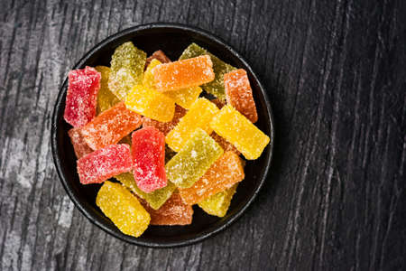 Jelly gummy candy pieces in dark bowl on a wooden tableの写真素材