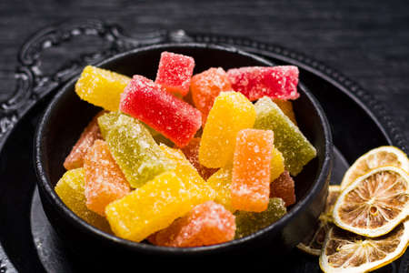 Jelly gummy candy pieces in dark bowl on a wooden tableの写真素材