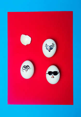 White eggs with drawn faces on red background top view