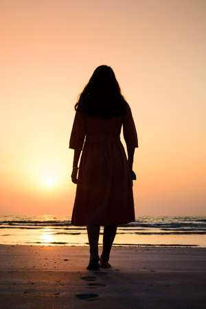 Girl walking on the beach at sunset back viewの写真素材