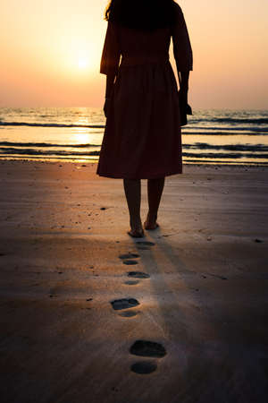 Girl walking on the beach at sunset back viewの写真素材