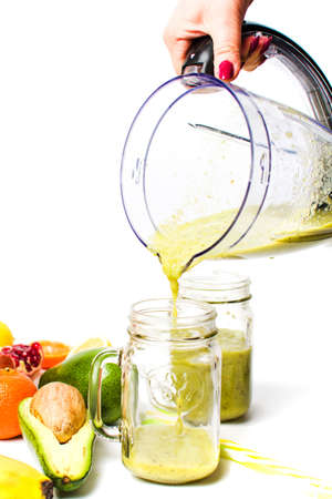 Woman pouring avocado smoothie from a blender in a jarの写真素材