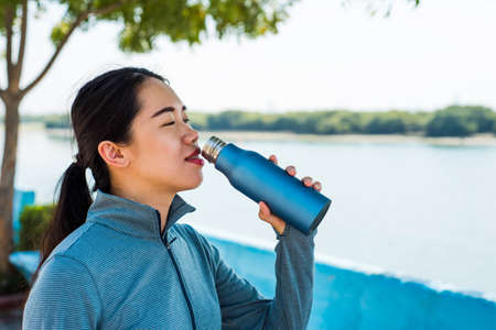 Female hydrating after workout in the park by the waterの写真素材