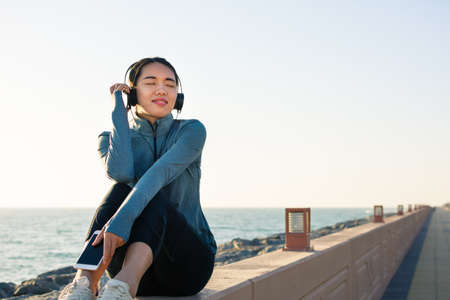 Girl listening to music sitting by the seaside and enjoying sunny dayの写真素材