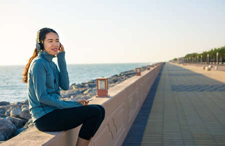 Girl listening to music sitting by the seaside and enjoying sunny dayの写真素材