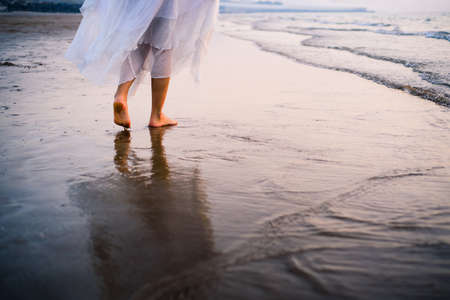Girl walking on the beach wearing white dress at sunsetの写真素材