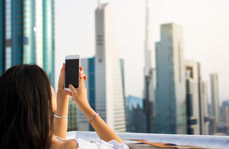 Girl taking picture of Dubai cityscape by phoneの写真素材